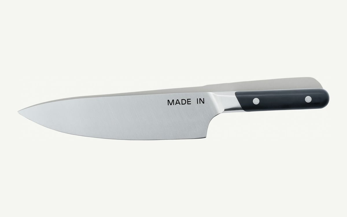 Made In chef knife on an off-white ground: a tall stainless blade stamped MADE IN, tip to the left, black handle with two rivets