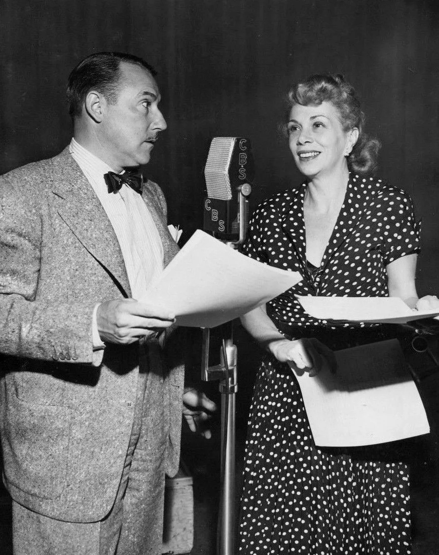Gale Gordon and Bea Benaderet hold scripts on either side of a studio microphone.
