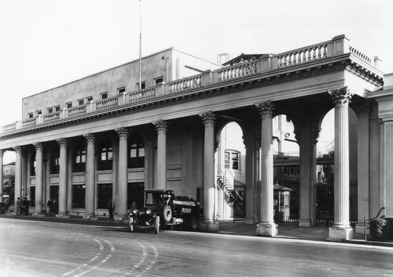 Historic black-and-white view of a columned studio building with an early gasoline truck in front.