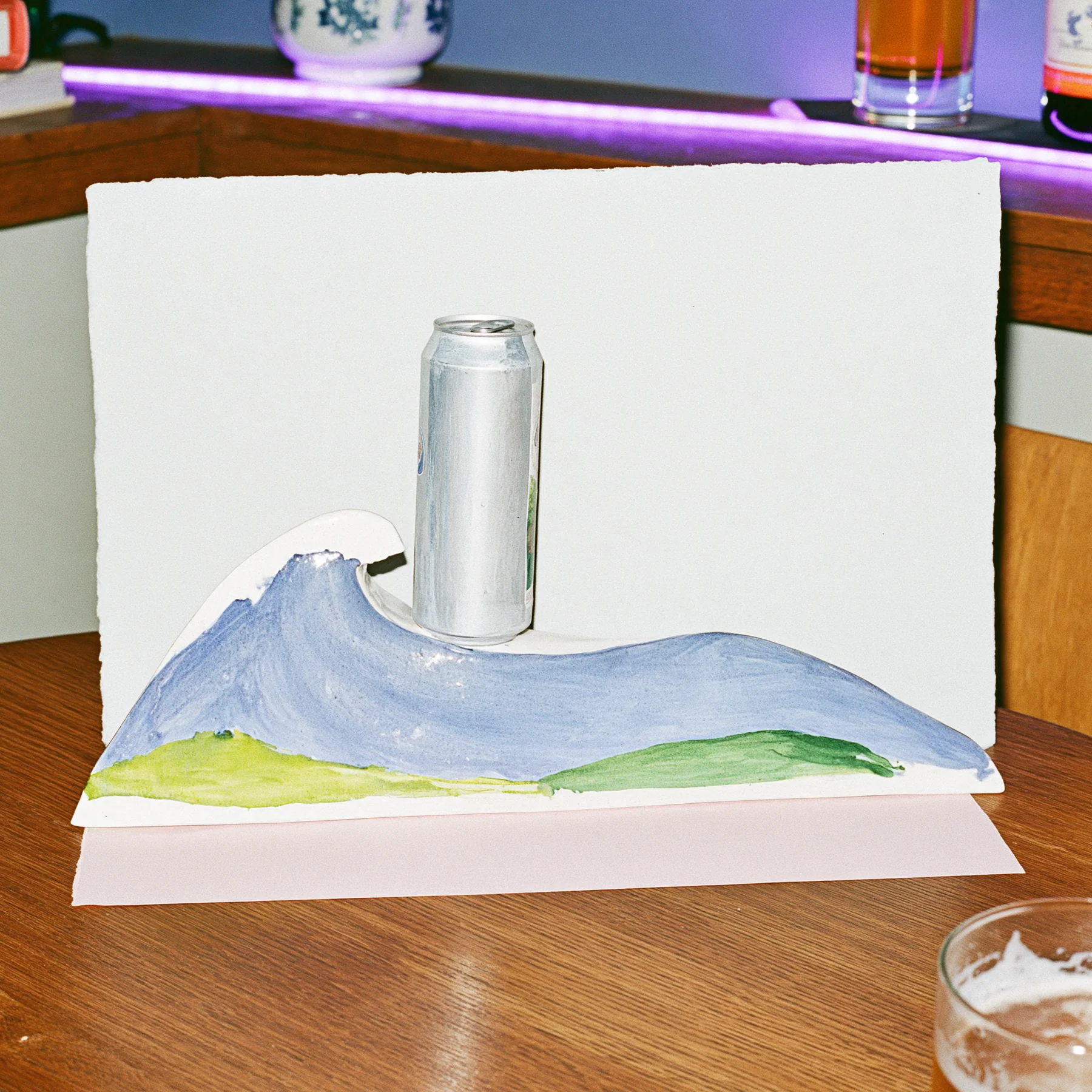 A silver can stands on a handmade paper ocean wave model in a neon-lit room