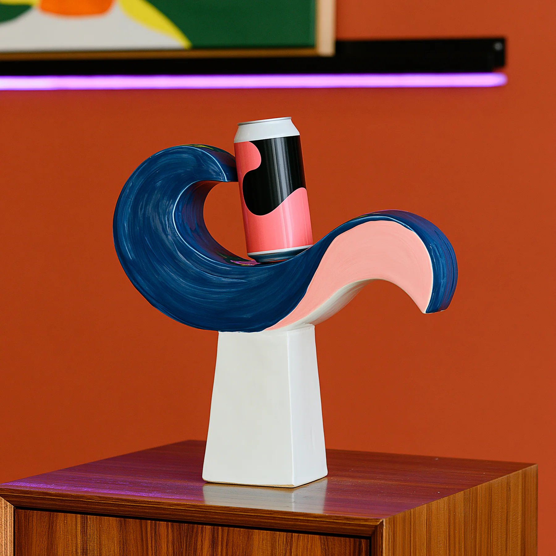 A pink can balances on a cobalt swan-shaped ceramic sculpture against a persimmon wall